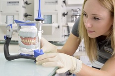 Eine junge Zahntechnikerin mit Gummihandschuhen arbeitet an einem Gebiss