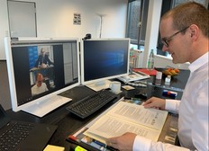 Kultusminister Tonne sitzt an seinem Schreibtisch, vor ihm der unterschriebene Kooperationsvertrag zu den Kinderrchten, auf dem Monitor vor ihm in der oberen Hälfte der andere Unterzeichner, Graf Waldersee, in der unteren Hälfte der Minister