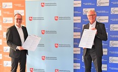 Kultusminister Grant Hendrik Tonne (links) und der LSB-Vorstandsvorsitzenden Reinhard Rawe vor drei verschiedenen RollUps stehend, mit Urkunde in der Hand