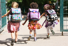 Drei Kinder mit Schulranzen laufen aufs Schulgelände
