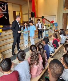 Minister Tonne mit Kindern in der Schulaula vor Publikum.