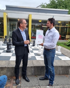 Minister Tonne und Schulleiter Eichler stehen auf dem Schulhof der pestalozzi-Schule vor Publikum und Minister übergibt die Urkunde