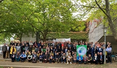 Gruppenfoto der ausgezeichneten Schulen draußen vor der Universität, Fassade bewachsen, 2 Bäume.