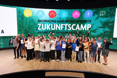 Gruppenbild mit Menschen auf einer Bühne, die begeistert ihre Arme hoch strecken.