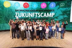 Gruppenbild mit Menschen auf einer Bühne, die begeistert ihre Arme hoch strecken.