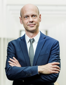 Photo eines Mannes im Stehen mit verschränkten Armen