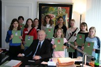 Minister sitzt am Schreibtisch, um ihn herum stehen die Mädchen, die am Girls