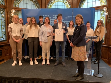 Gruppenfoto auf einer kleinen Bühne mit Ministerin und der Urkunde des Schülerfriedenspreises