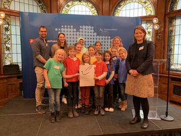 Gruppenfoto auf einer kleinen Bühne mit Ministerin und der Urkunde des Schülerfriedenspreises