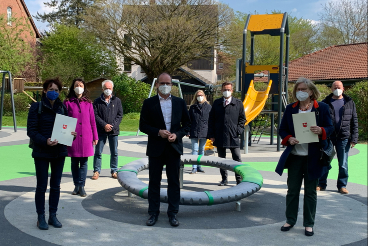 Grupppe mit Menschen stehen draußen in einem Schulgarten, ein Mann überreicht ein papier.