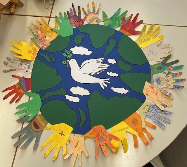 Hände aus Papier umschließen eine Weltkugel it Friedenstaube