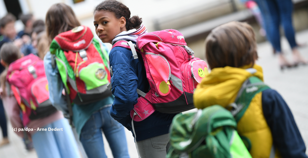 Kinder stehen mit Ranzen auf dem Schulhof