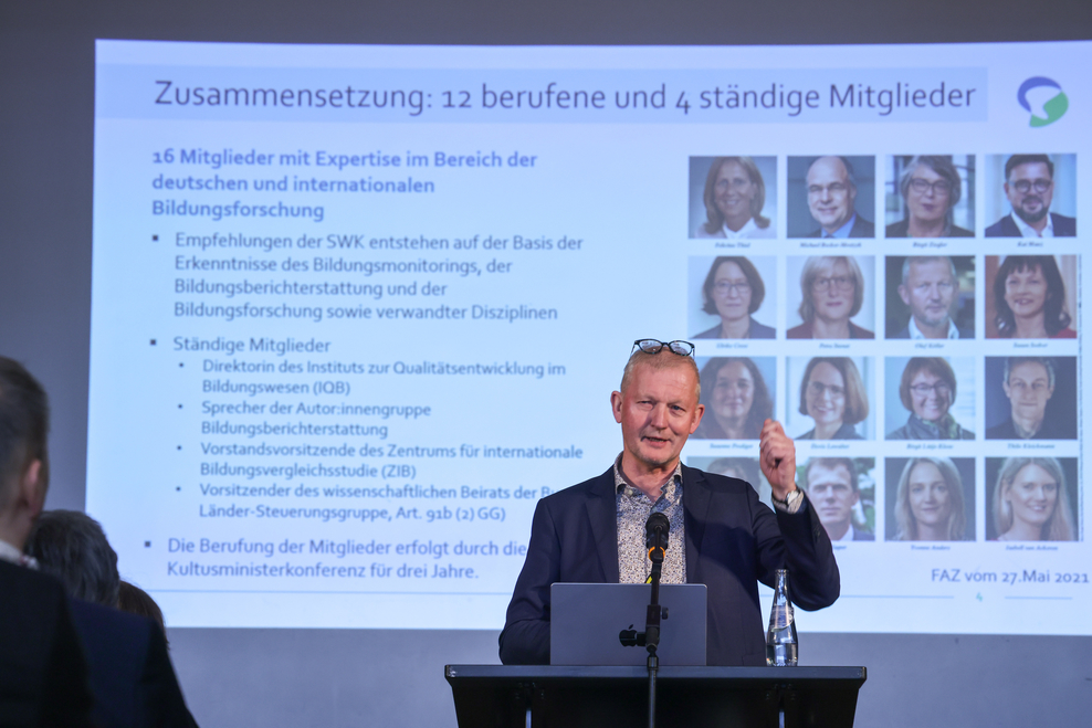 Ein Mann am Rednerpult spricht - im Hintergrund ewrscheinen Infos auf einer Leinwand.