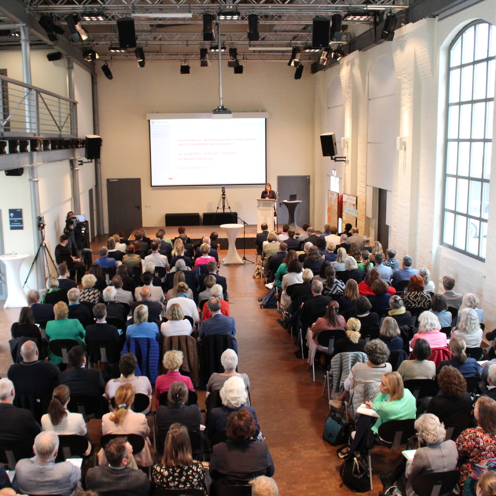 Menschen im Saal, sitzend, eine Frau am Pult trägt vor