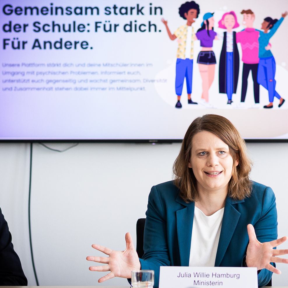 Eine Frau sitzt am Tisch und erklärt estwas mit Armgestiken.