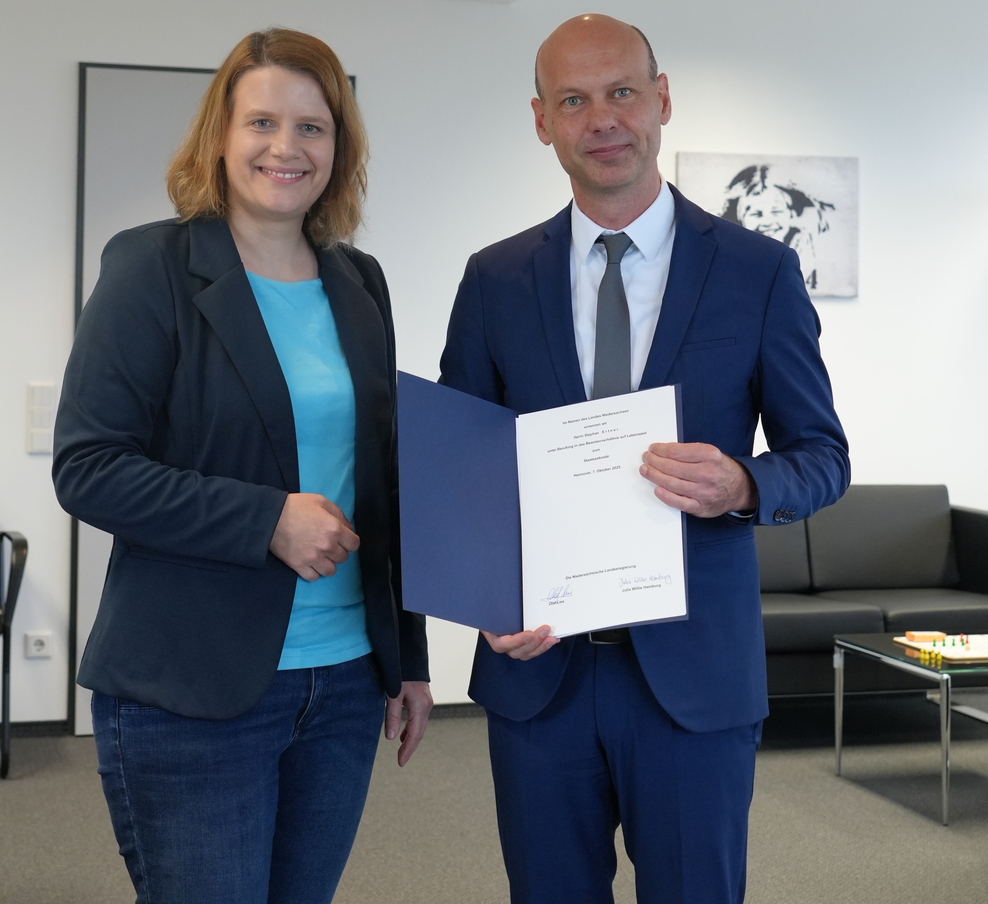 eine Frau und ein Mann stehen nebeneinander und der Mann hält eine Urkunde in der Hand.