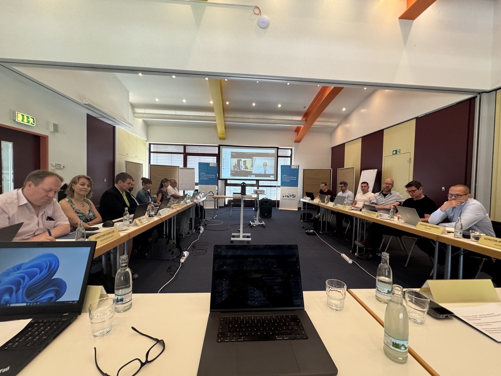 Konferenzraum mit Menschen an den Tischen, im Vordergrund ein Laptop